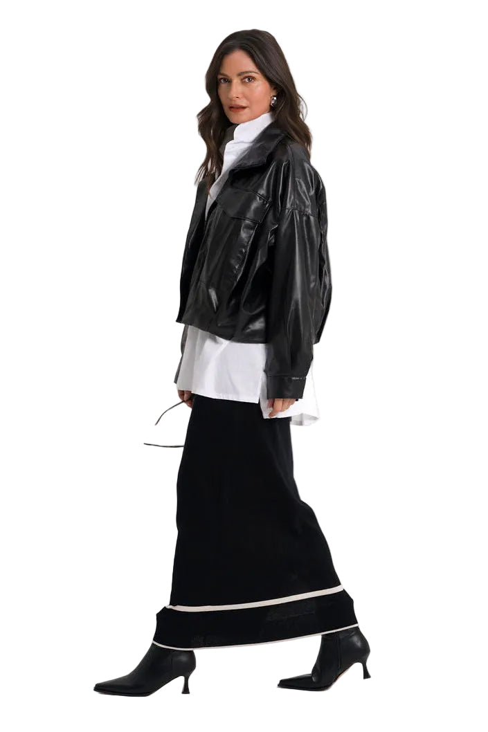 A woman modeling a black faux-leather moto jacket over a white shirt and a long black skirt with a white stripe, paired with black pointed-toe heels, on a solid white background.