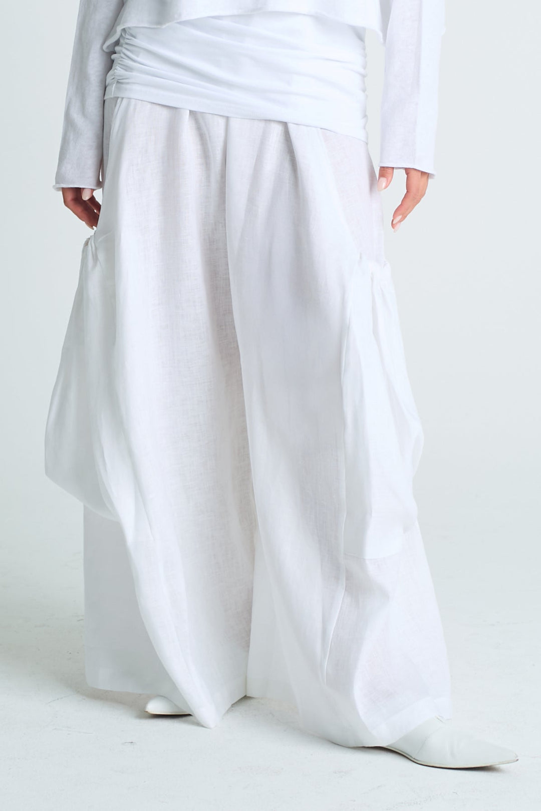 Person wearing a loose-fitting white linen pants and top on a plain background