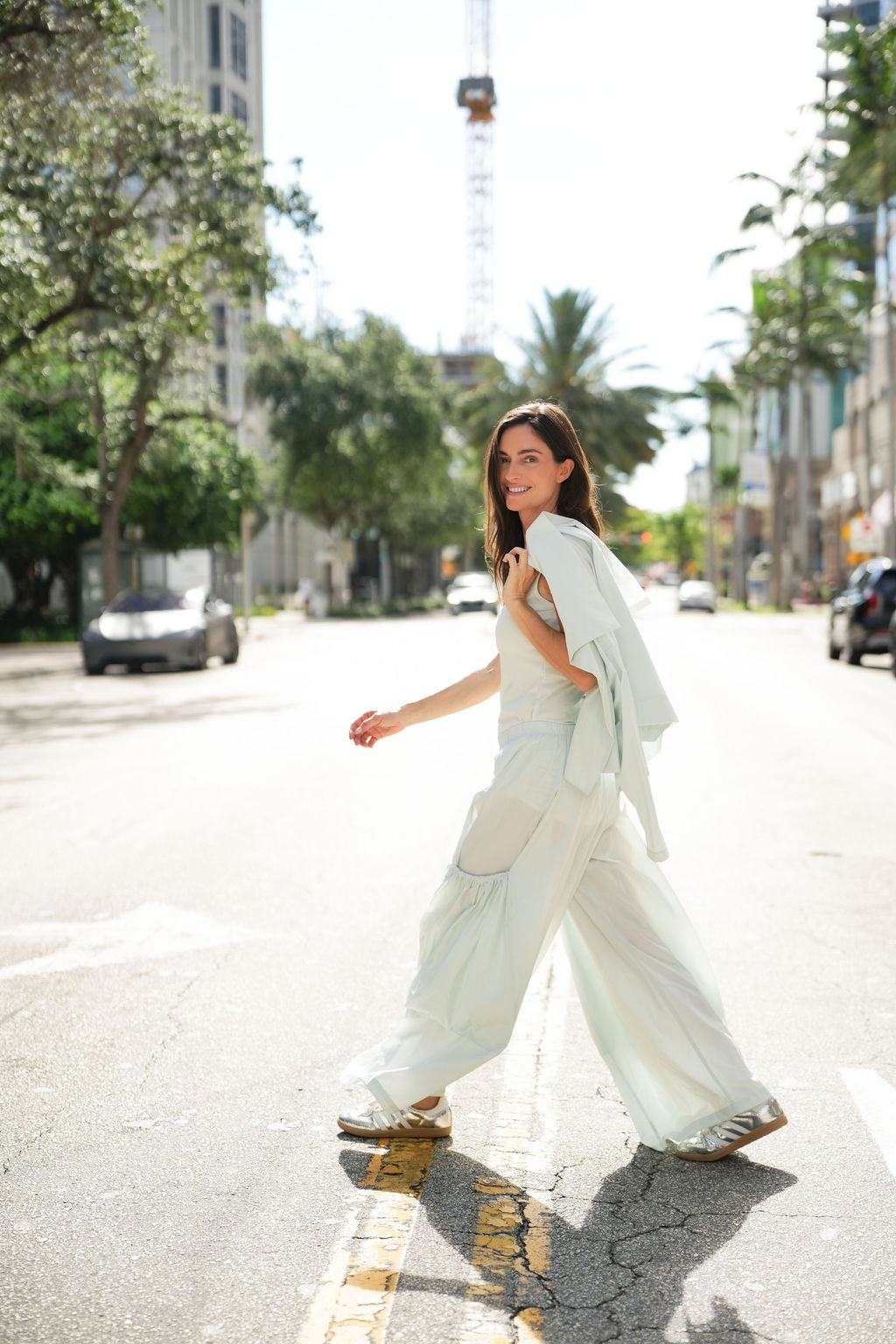 Woman in a mint outfit and big pocket pants walking on a city street with trees and buildings in the background.