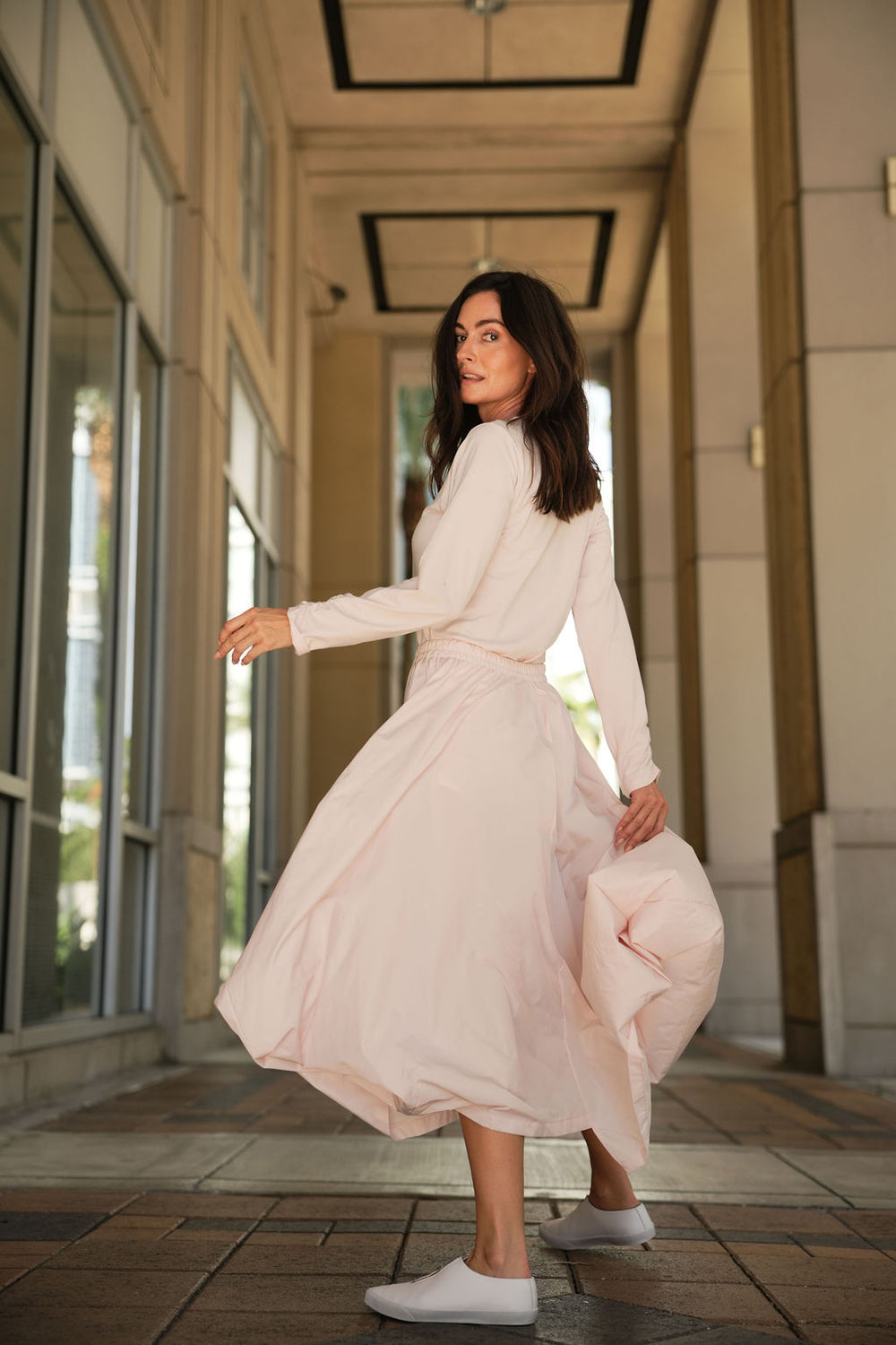Woman in a pink blush skirt standing in an outdoor setting near large windows.