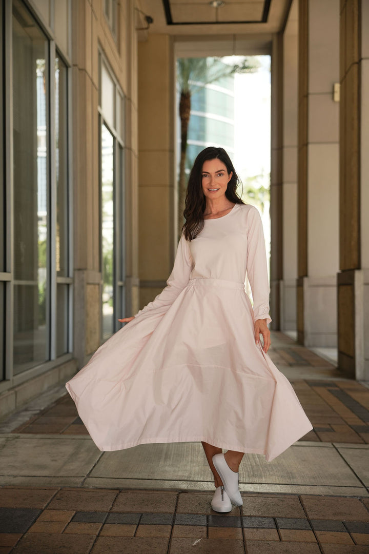 Woman in a pink blush nylon skirt standing in an outdoor setting with buildings in the background