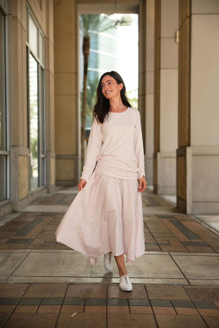 Woman smiling in a pink blush outfit standing in an outdoor setting with architectural elements.
