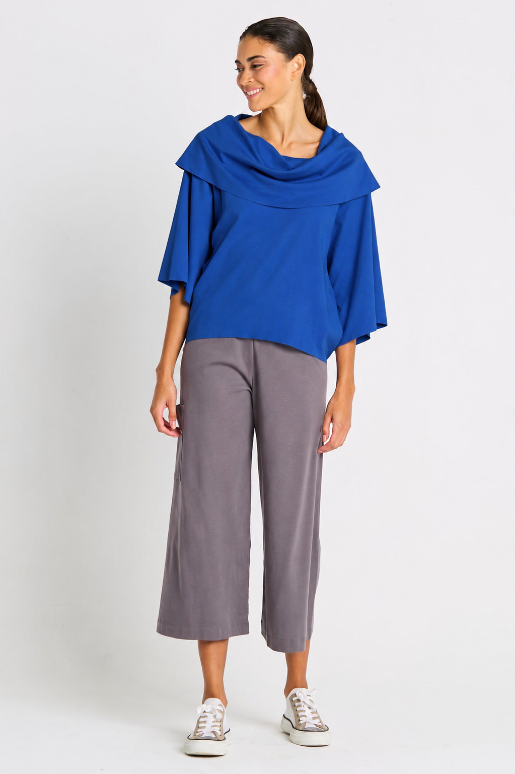 Woman wearing a blue jackie o pima cotton top and gray pants on a white background