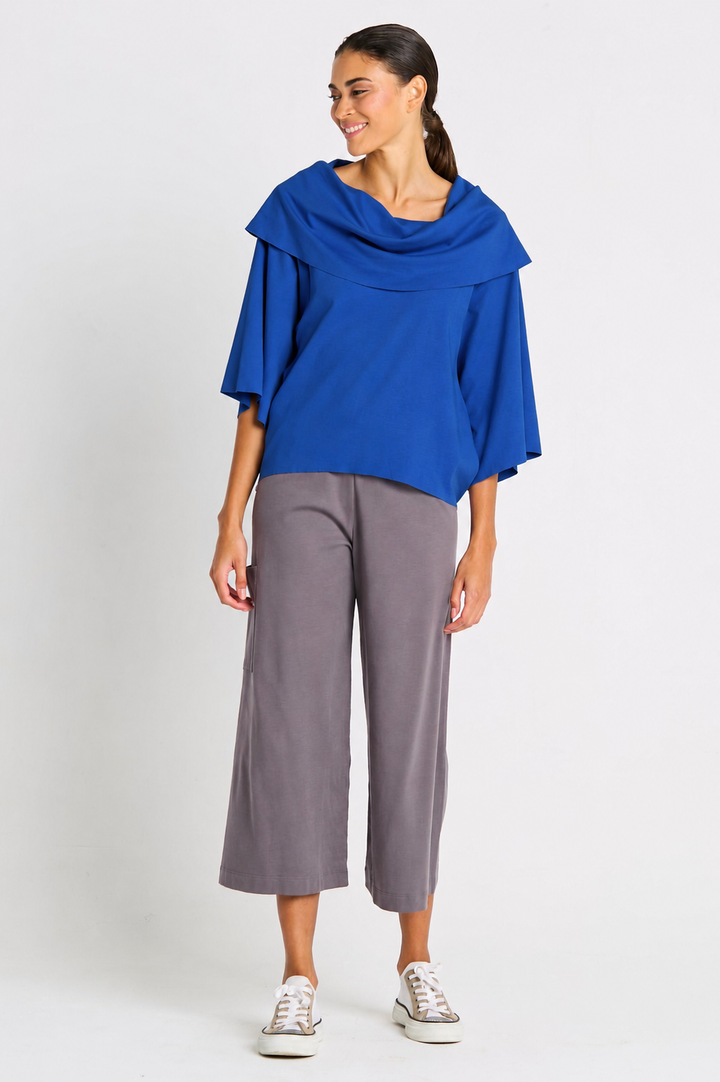 Woman wearing a blue jackie o pima cotton top and gray pants on a white background