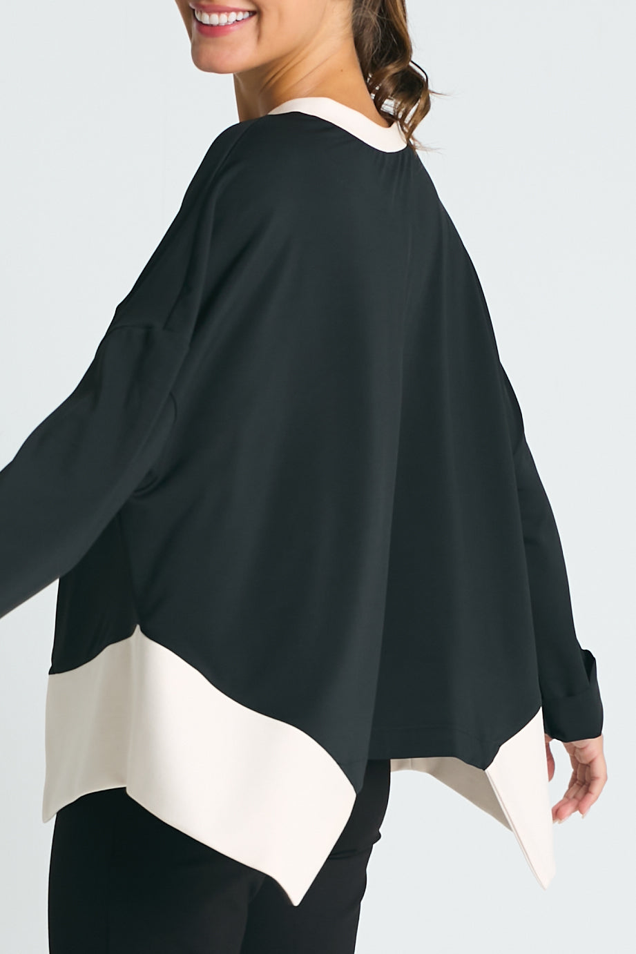 A woman wearing a matte jersey paneled top with long sleeves. The top has a black color with a white panel at the bottom.