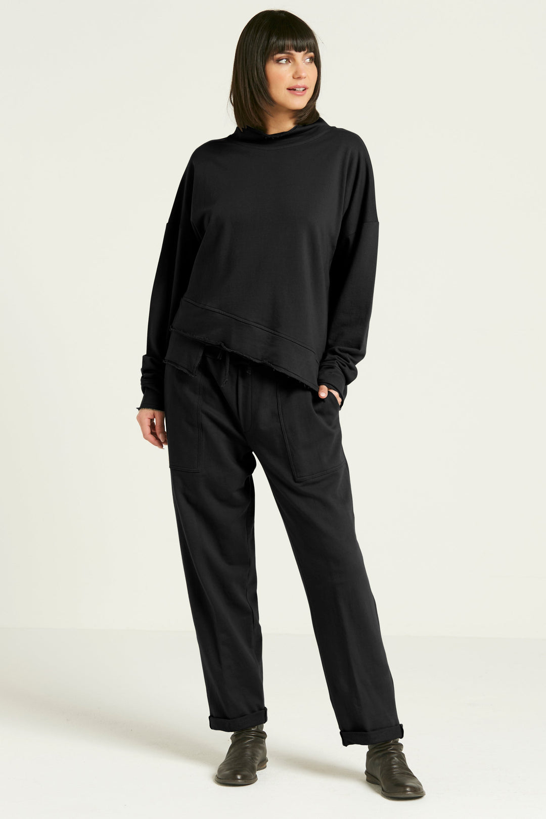A person standing against a white background, wearing black French Terry luxury sweatpants with a drawstring closure and pockets, paired with a black top and gray shoes.