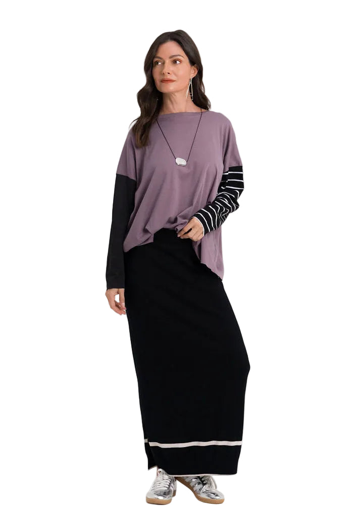 A woman modeling a 100% pima cotton long-sleeve top with a lavender-purple and black color-blocked design, featuring black-and-white striped sleeves, paired with a long black skirt, against a plain white studio background.
