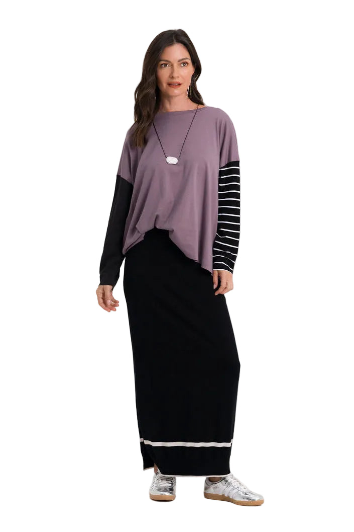 A woman modeling a 100% pima cotton two-tone long-sleeve top with a dusty purple body and black sleeves featuring white stripes, paired with a long black skirt, against a plain white studio background.