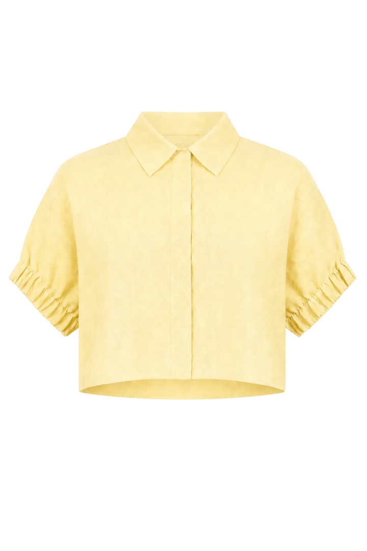 A 100% linen pale yellow cropped short-sleeve button-up shirt with a pointed collar and gathered ruffled cuffs, shown against a plain white background.