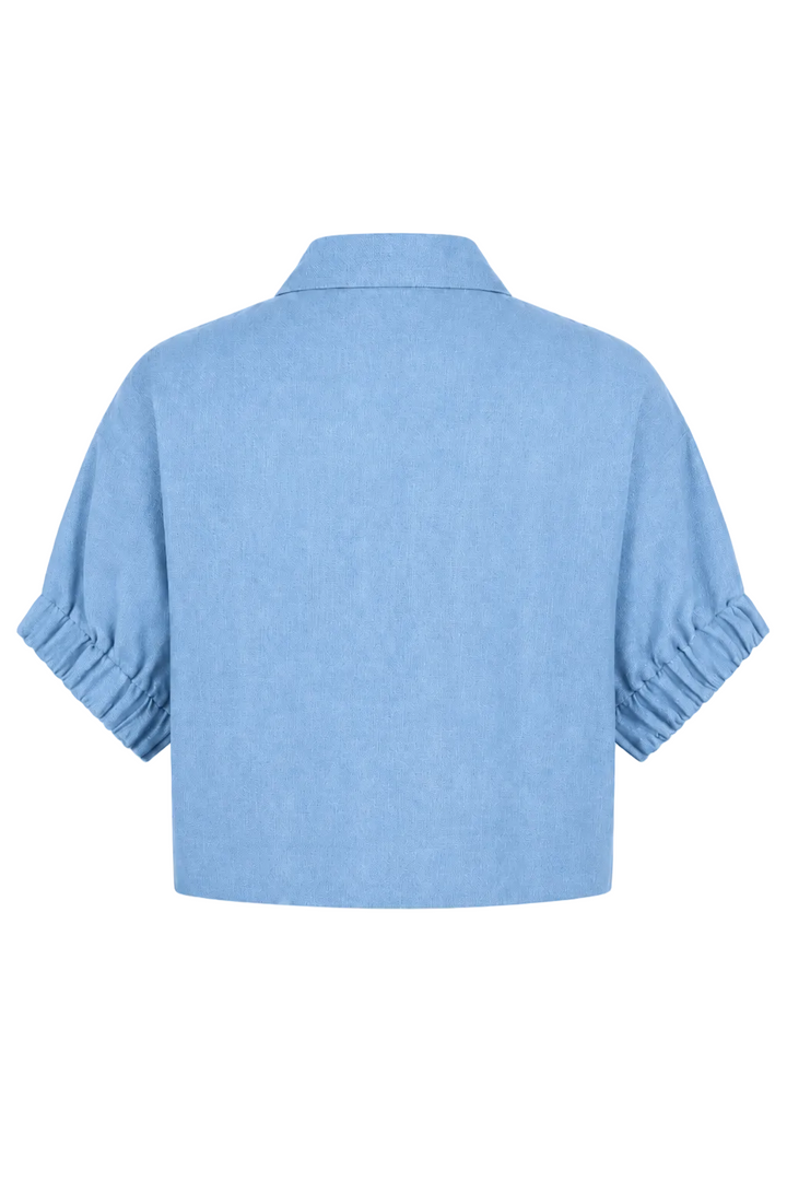 A 100% linen light blue cropped short-sleeve shirt with gathered ruffle details on the sleeves, shown from the back against a plain white background.