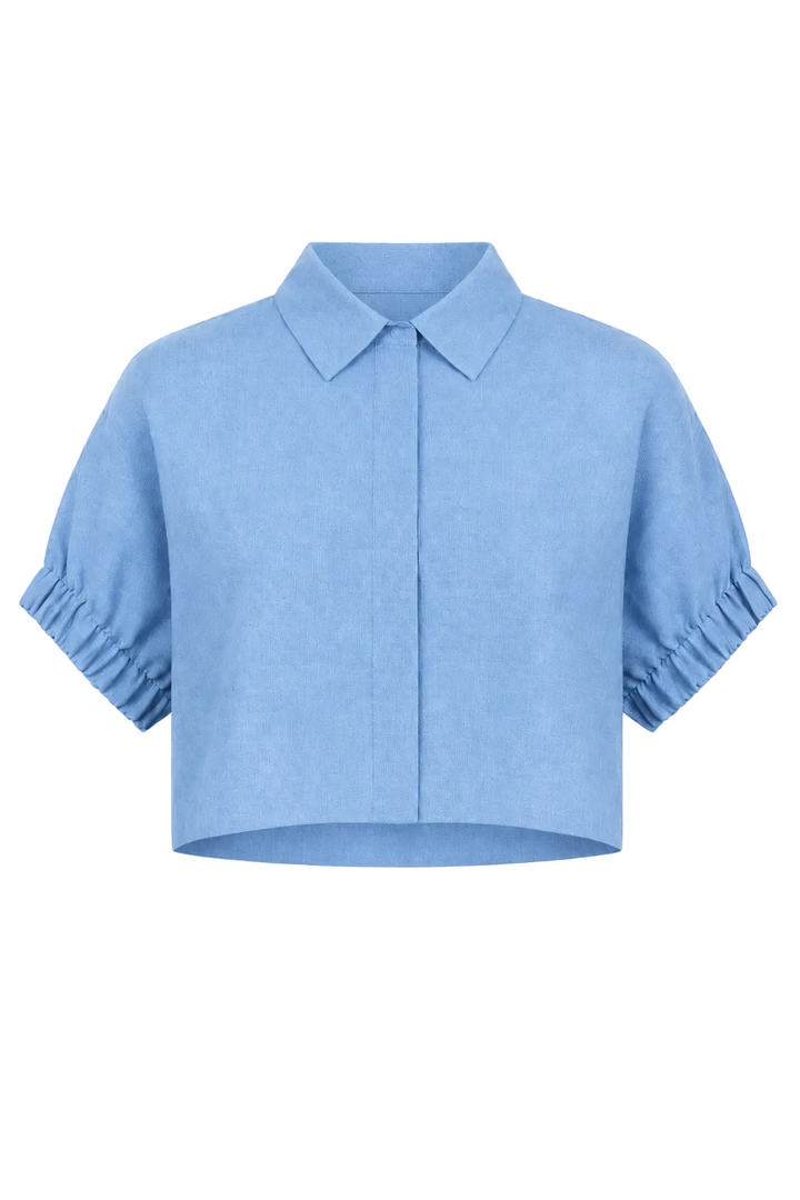 A 100% linen light blue cropped short-sleeve blouse with a pointed collar, front button placket, and gathered ruffled cuffs, shown on a plain white background.