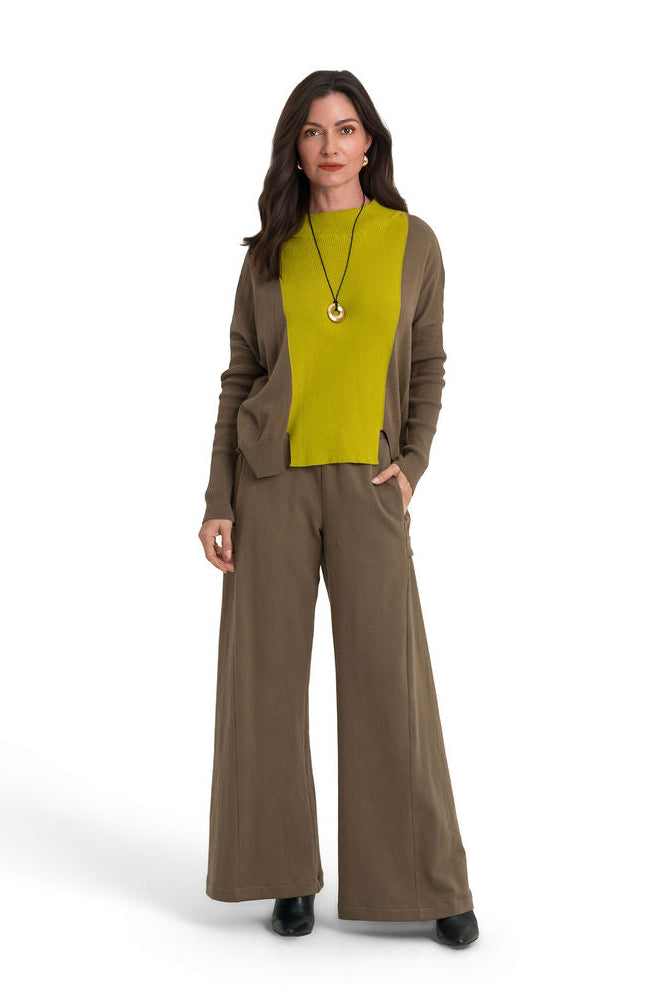 A woman modeling a matching two-piece outfit consisting of a turtle long-sleeve pima cotton sweater and wide-leg 100% cotton french terry pants, layered over a bright yellow-green knit top. She is standing against a seamless white studio background.