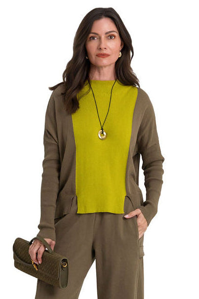 A woman modeling a color-block pima cotton knit sweater with olive green side panels and sleeves, a bright yellow-green center panel, and matching olive green trousers, holding a dark olive clutch against a plain white background.