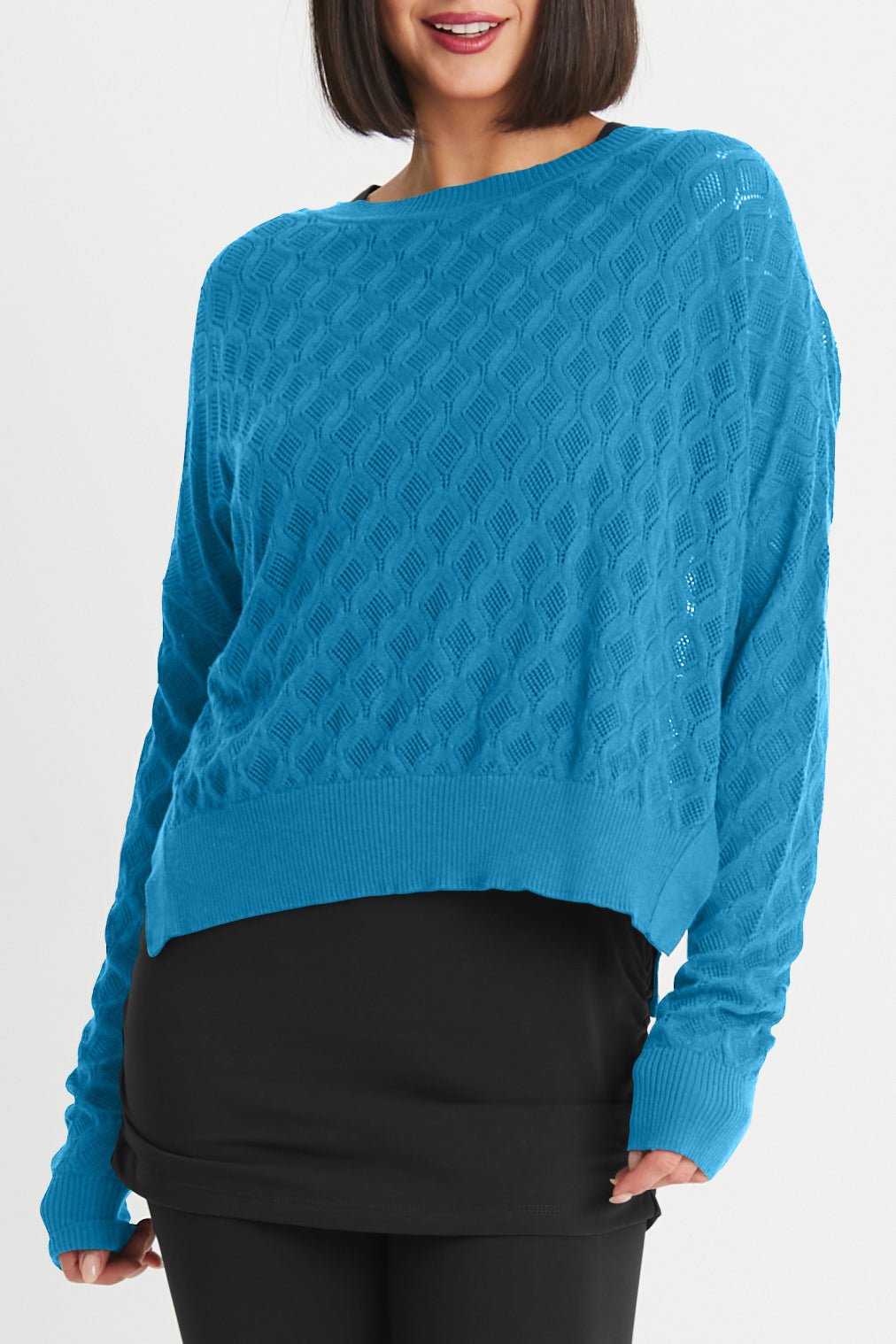 Woman wearing a blue cable knit sweater against a white background with black leggings