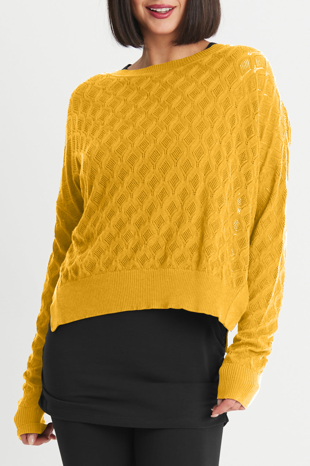 Woman wearing a mustard yellow cable knit sweater against a white background