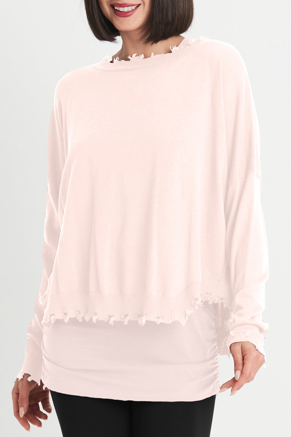 Woman wearing a light pink blouse with fringe details on a plain background