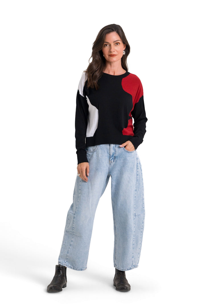 A woman modeling a 100% pima cotton color-blocked knit sweater with light-wash wide-leg jeans and black boots, standing against a solid white background.
