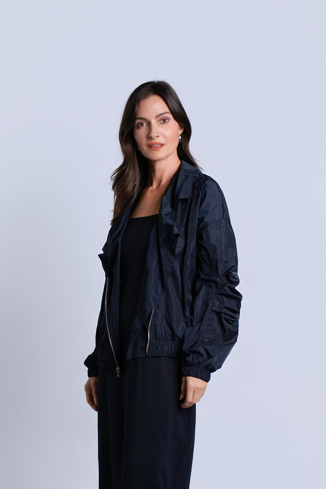A woman modeling a dark navy blue lightweight jacket over a black outfit, standing against a light gray studio background.