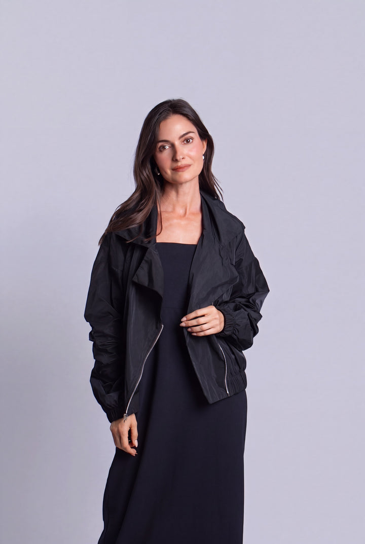 A woman modeling a black lightweight zip-front jacket over a black dress, standing against a plain light gray studio background.