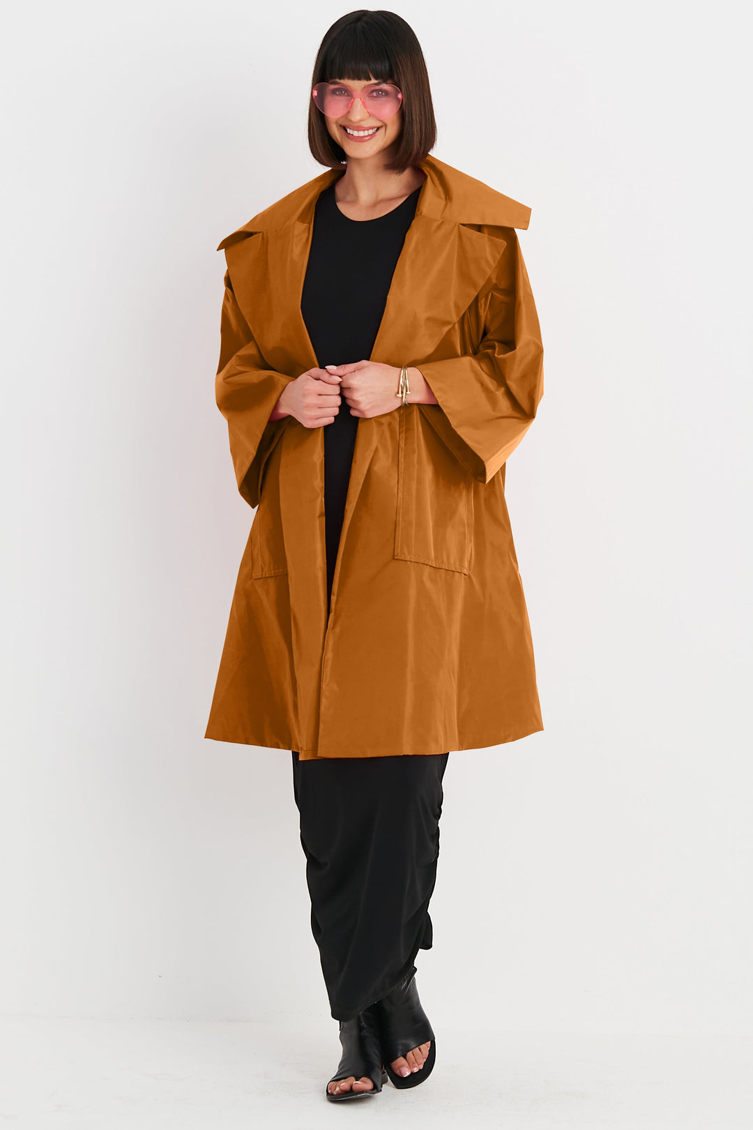 A female model wearing a blush nylon coat with a mandarin collar, oversized pockets, and three-quarter sleeves.