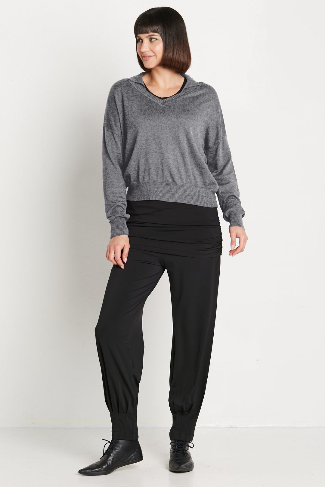 Woman wearing a gray sweater and black pants on a white background