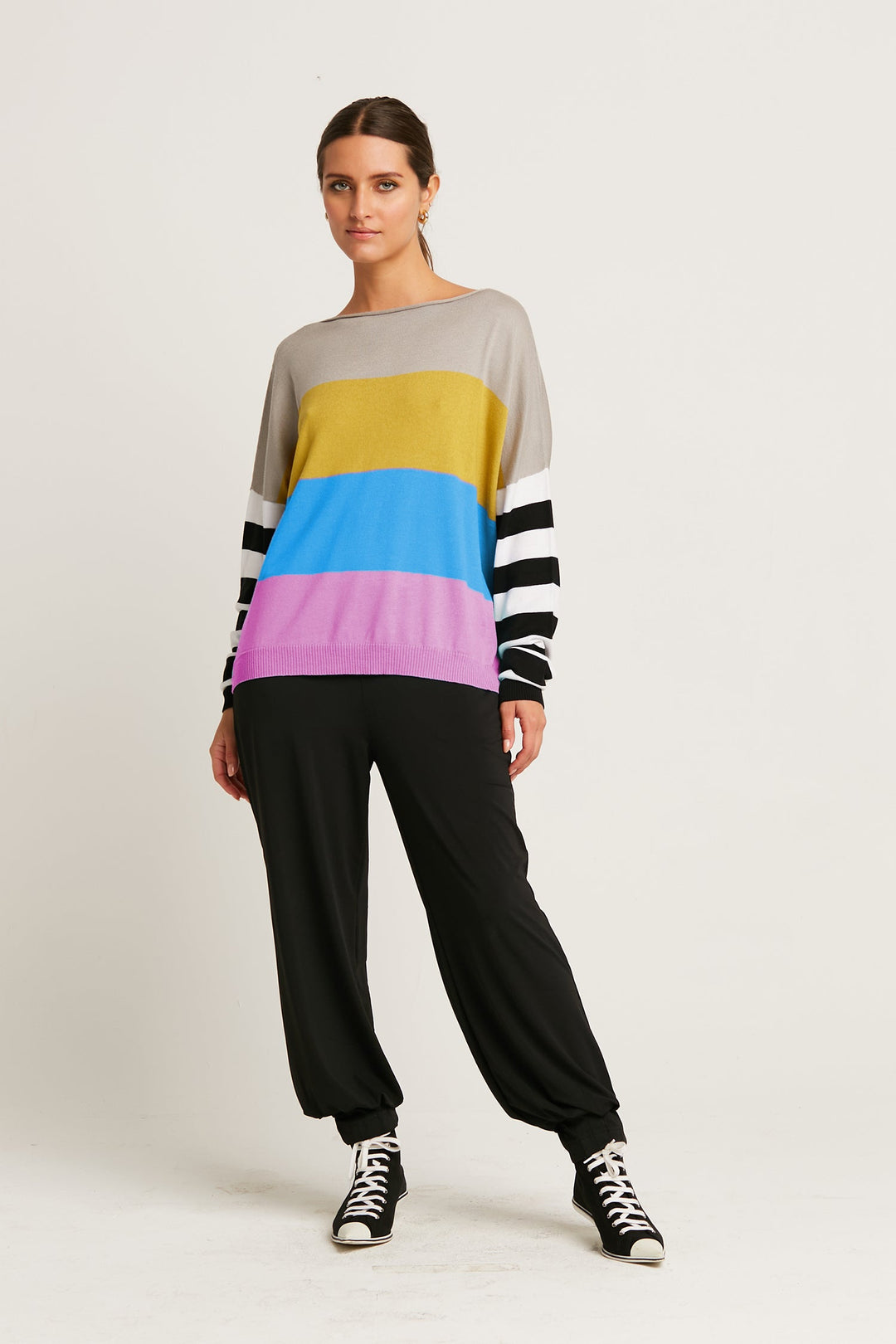 Person wearing a colorful striped sweater and black pants on a white background