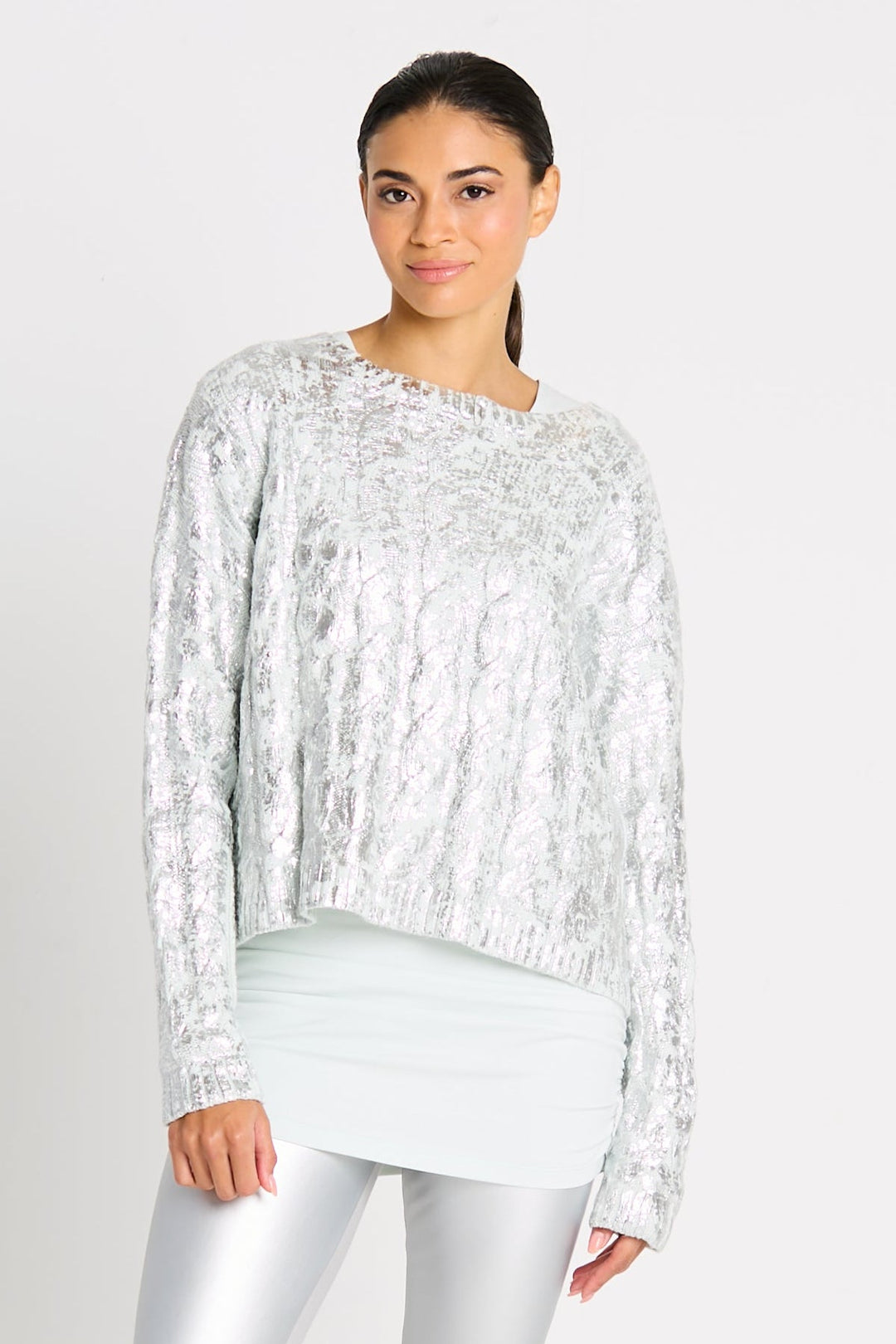 A woman wearing a pima cotton silver foil cable-knit crewneck sweater with a boxy fit and cropped design, paired with silver leggings.