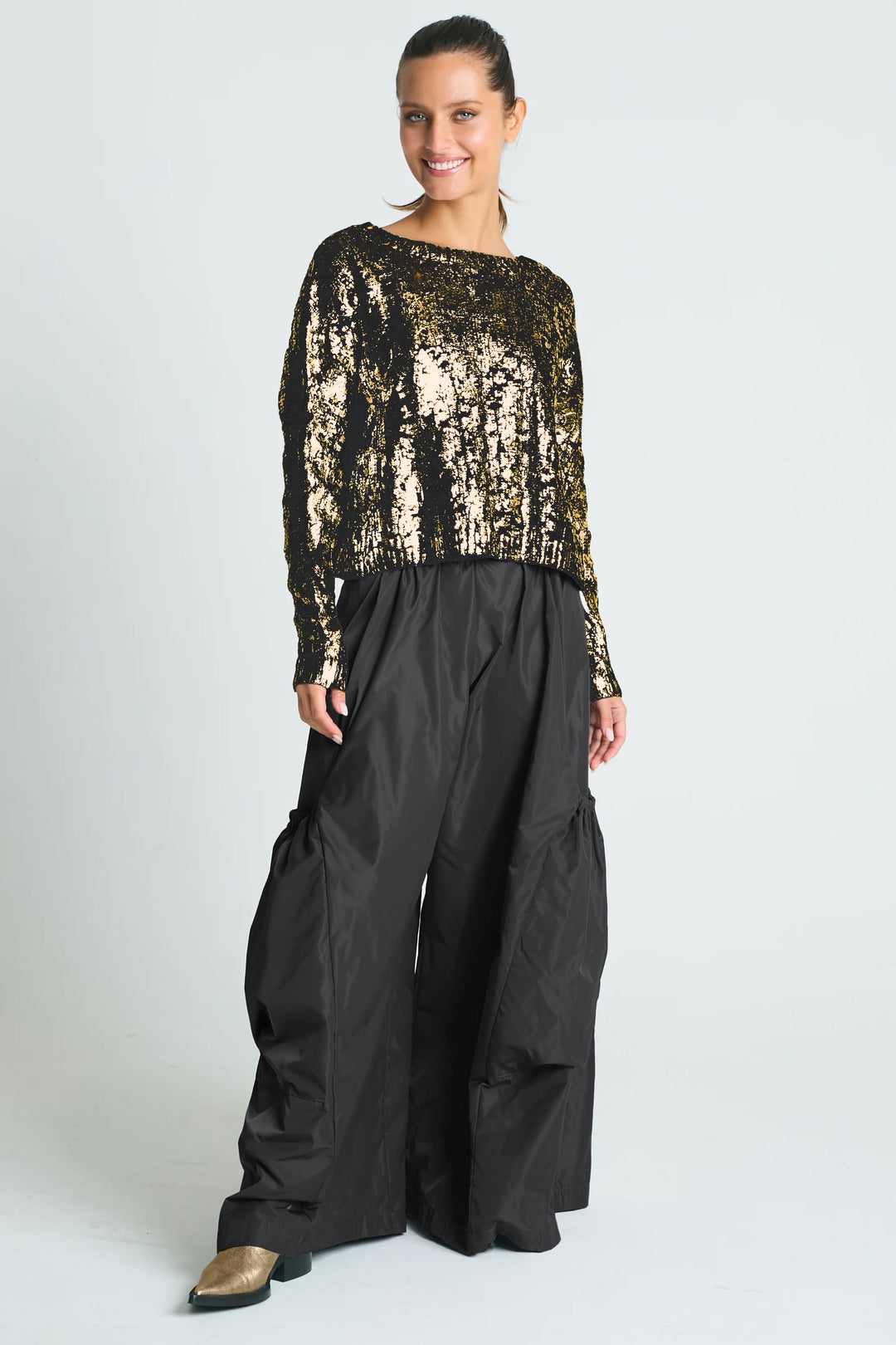 A woman wearing a pima cotton silver foil cable-knit crewneck sweater with a boxy fit and cropped design, paired with gray trousers.