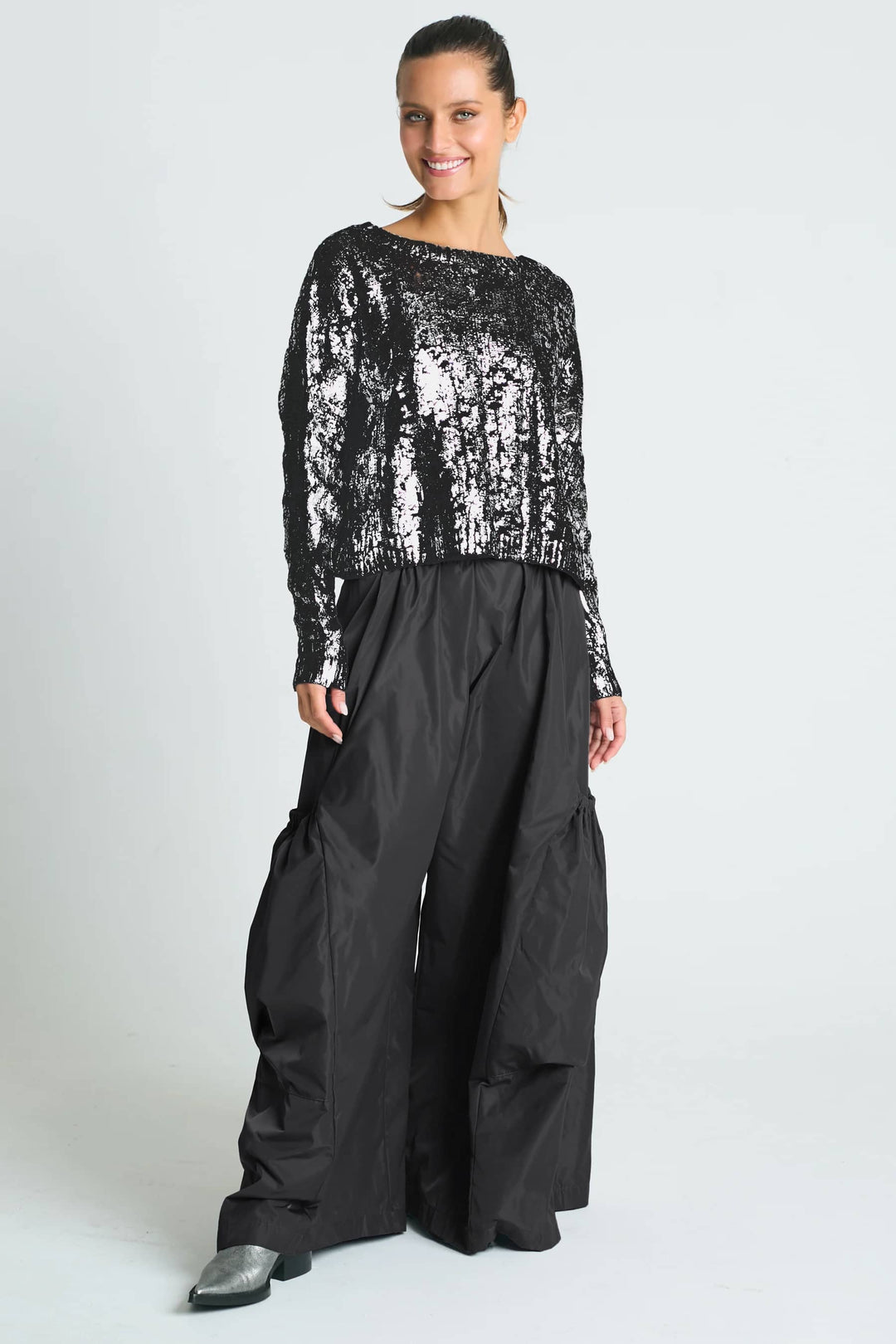 A woman wearing a pima cotton black foil cable-knit crewneck sweater with a boxy fit and cropped design, paired with gray trousers.
