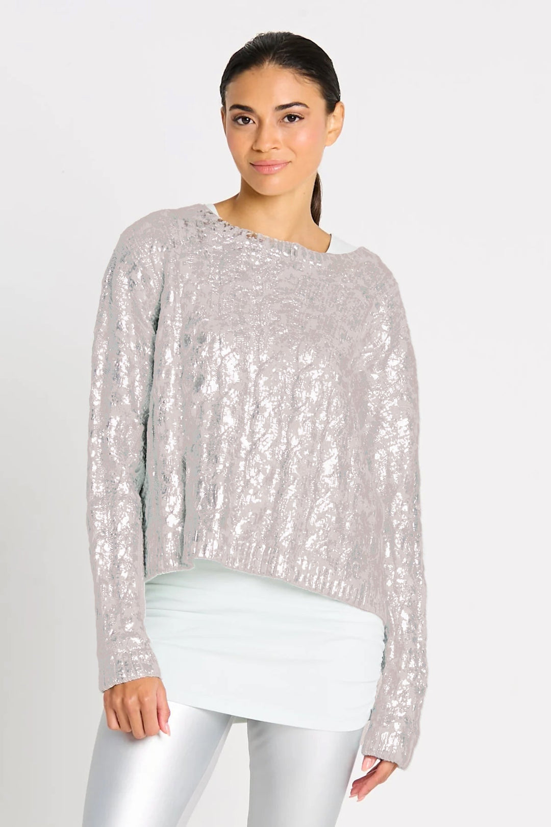 A woman wearing a pima cotton silver foil cable-knit crewneck sweater with a boxy fit and cropped design, paired with silver trousers.