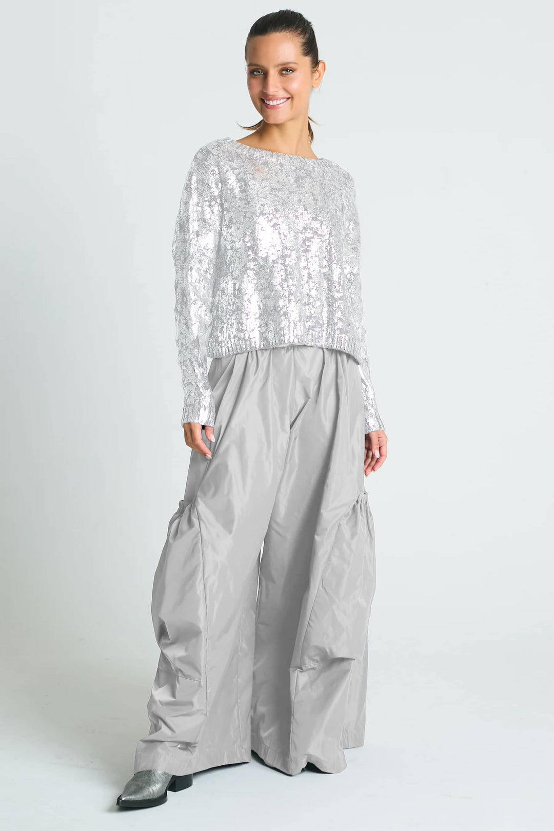 A woman wearing a pima cotton black and gold foil cable-knit crewneck sweater with a boxy fit and cropped design, paired with black trousers.