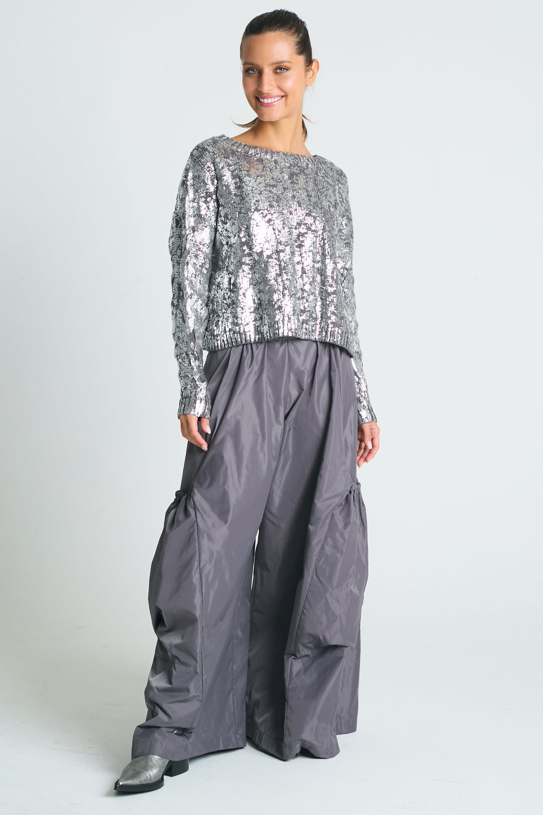 A woman wearing a pima cotton silver foil cable-knit crewneck sweater with a boxy fit and cropped design, paired with gray trousers.