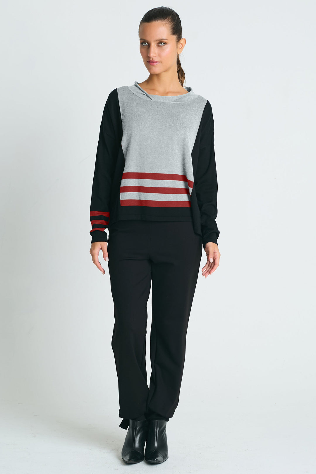 Woman wearing a gray and black pima cotton sweater with red stripes and black pants on a white background