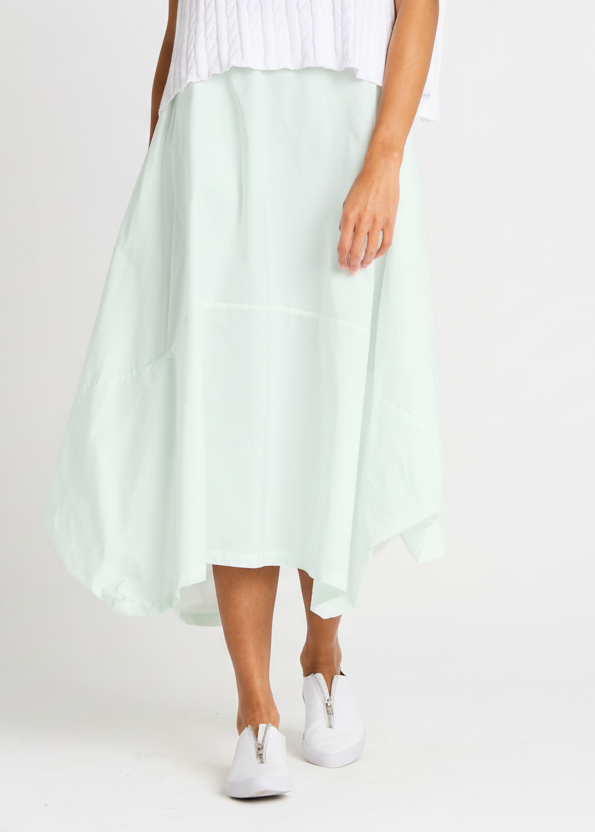 Person wearing a light green skirt with white sneakers on a plain background