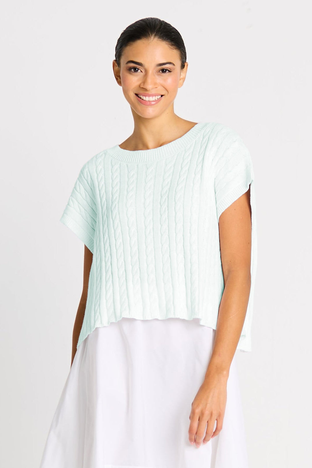 Woman wearing a light pink top and white pants on a plain background