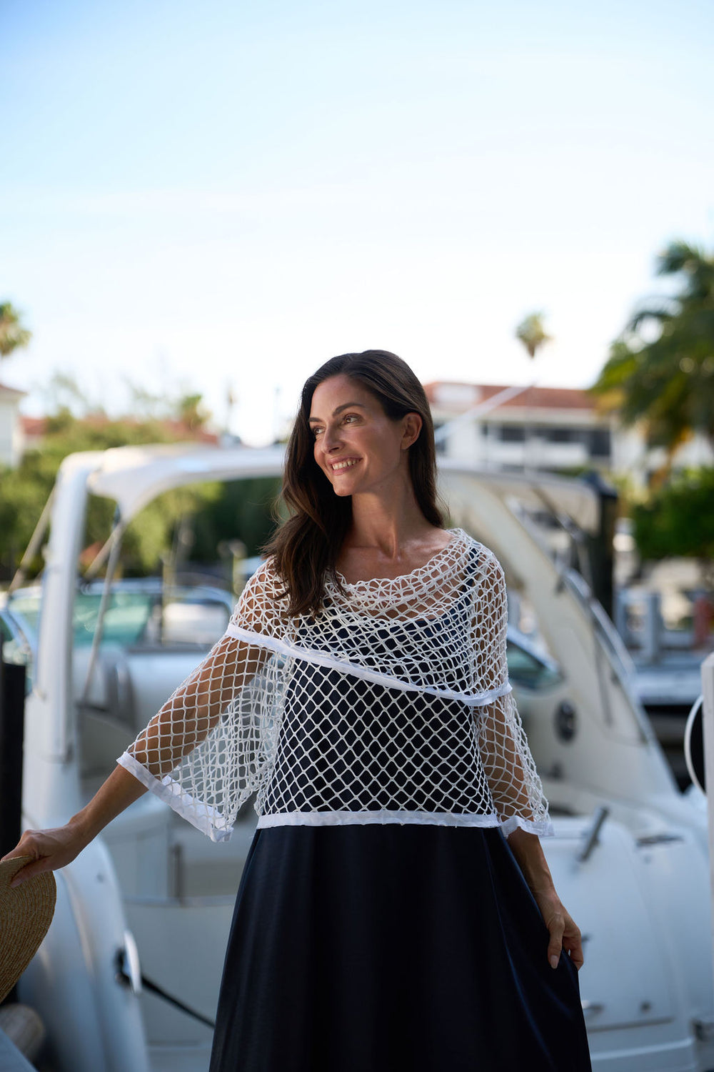 Woman wearing a white fishnet top and black skirt standing in front of a boat.