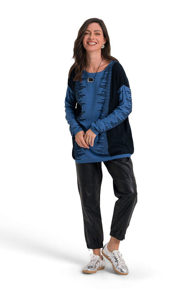 A woman modeling a blue and black patchwork pima cotton knit top with black cropped pants and white sneakers, standing against a solid white background.