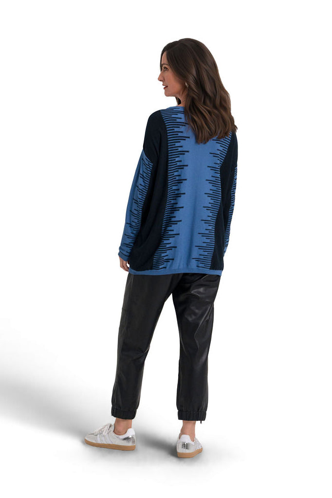 A woman is shown from the back wearing a blue and black textured pima cotton sweater, black pants, and white sneakers against a plain white background.