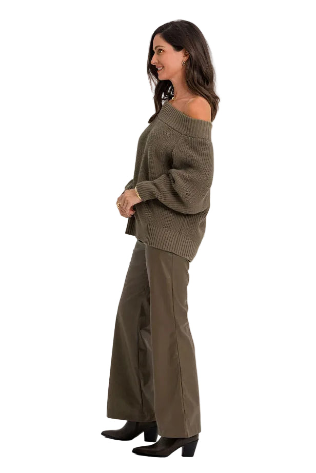 A woman stands in profile wearing an olive green off-the-shoulder knit top and matching wide-leg trousers against a plain white studio background.