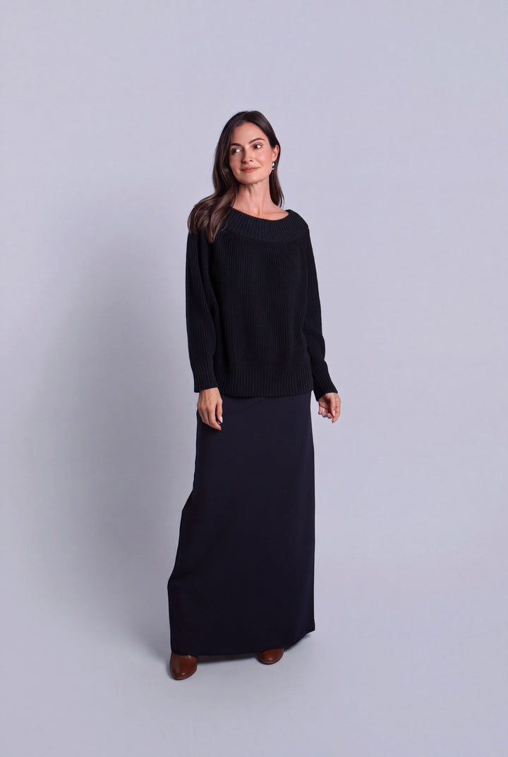 A woman modeling a black long-sleeve pima cotton knit top and matching black maxi skirt set against a light gray studio background.