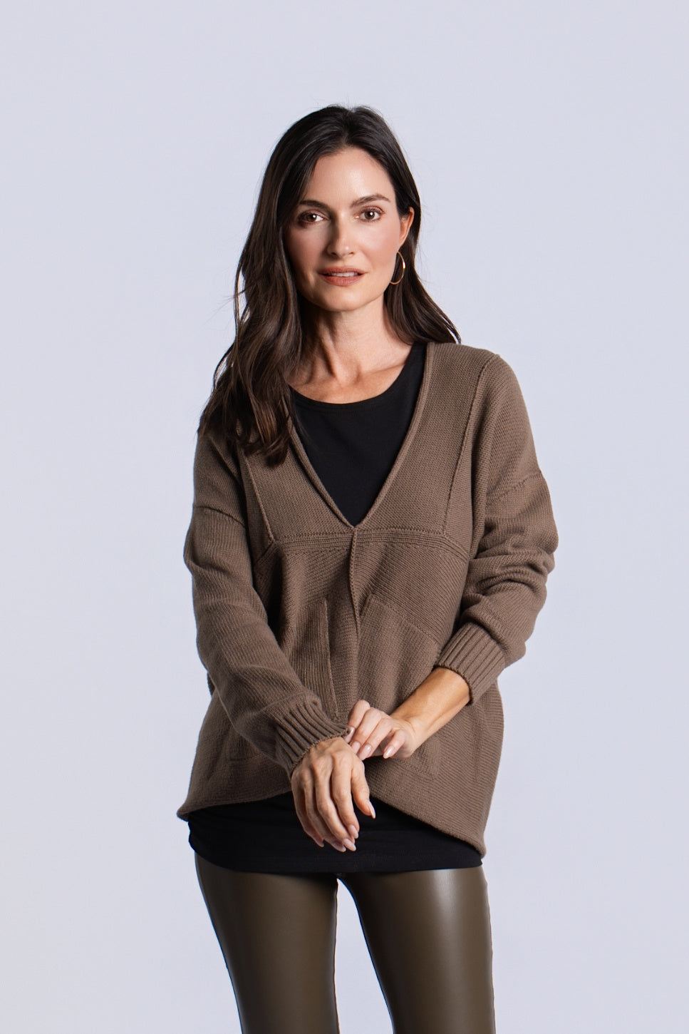 A woman modeling a turtle brown / green knit cardigan with a V-neck over a black top, paired with black leggings, against a light gray studio background.