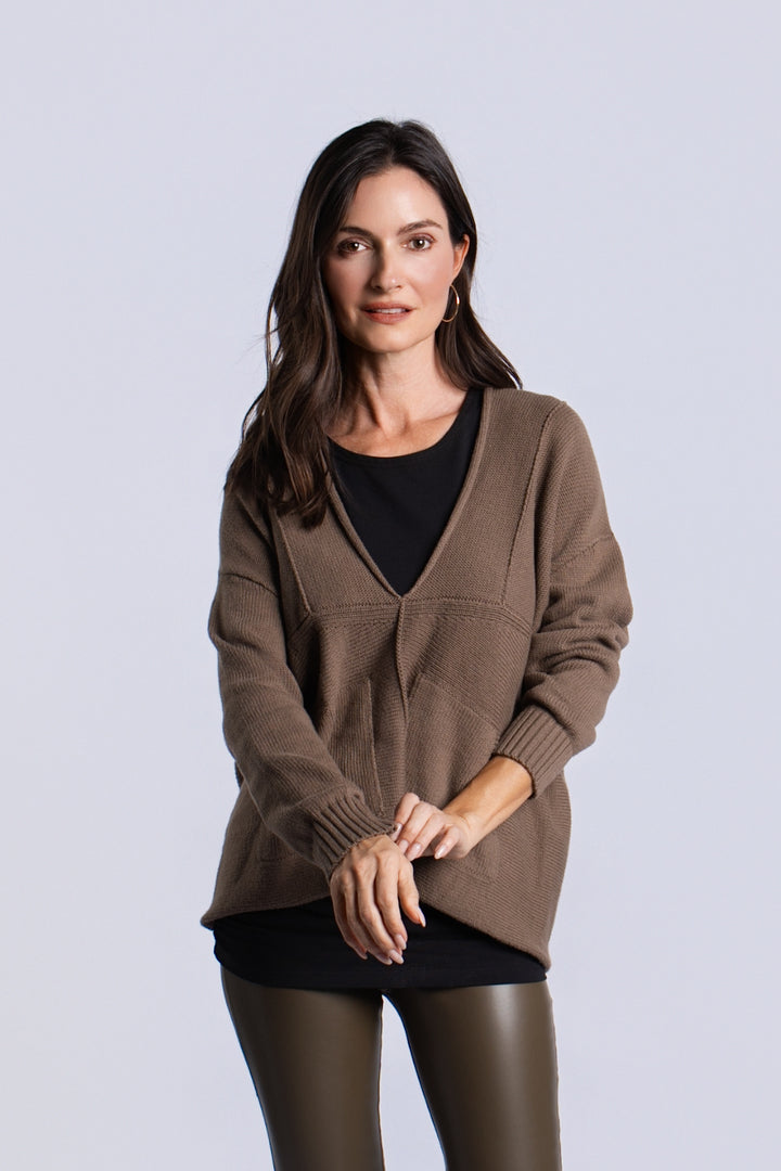 A woman modeling a turtle brown / green knit cardigan with a V-neck over a black top, paired with black leggings, against a light gray studio background.