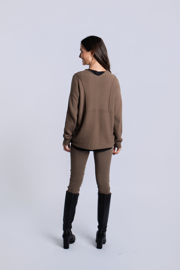 A woman is shown from the back wearing an oversized taupe-brown long-sleeve pima cotton cardigan, matching slim-fit pants, and black knee-high boots against a light gray studio background.