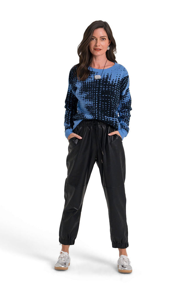 A woman modeling a blue and black patterned long-sleeve pima cotton top with black pants and silver sneakers, standing against a solid white background.