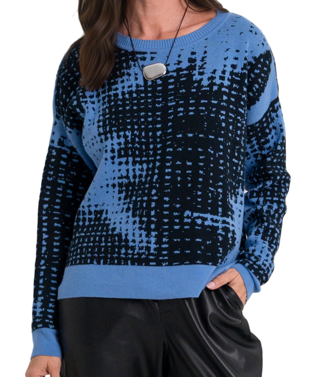 A woman wearing a blue and black patterned pima cotton knit sweater with a textured grid-like design, paired with black pants, against a plain white background.