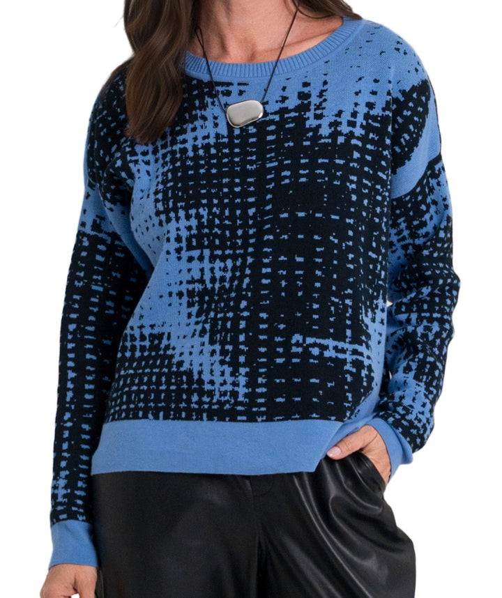 A woman wearing a blue and black patterned pima cotton knit sweater with a textured grid-like design, paired with black pants, against a plain white background.