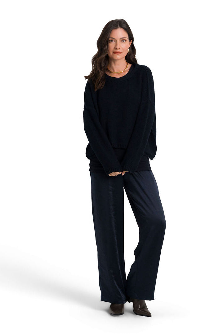 A woman modeling a dark navy blue pima cotton knit crewneck sweater and matching wide-leg trousers against a plain white studio background.