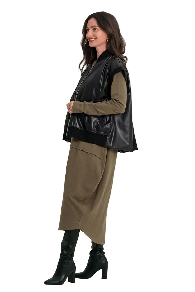 A woman modeling a black faux-leather vest over an 100% cotton olive green long-sleeve top and matching olive green skirt, paired with black heeled ankle boots, against a plain white studio background.