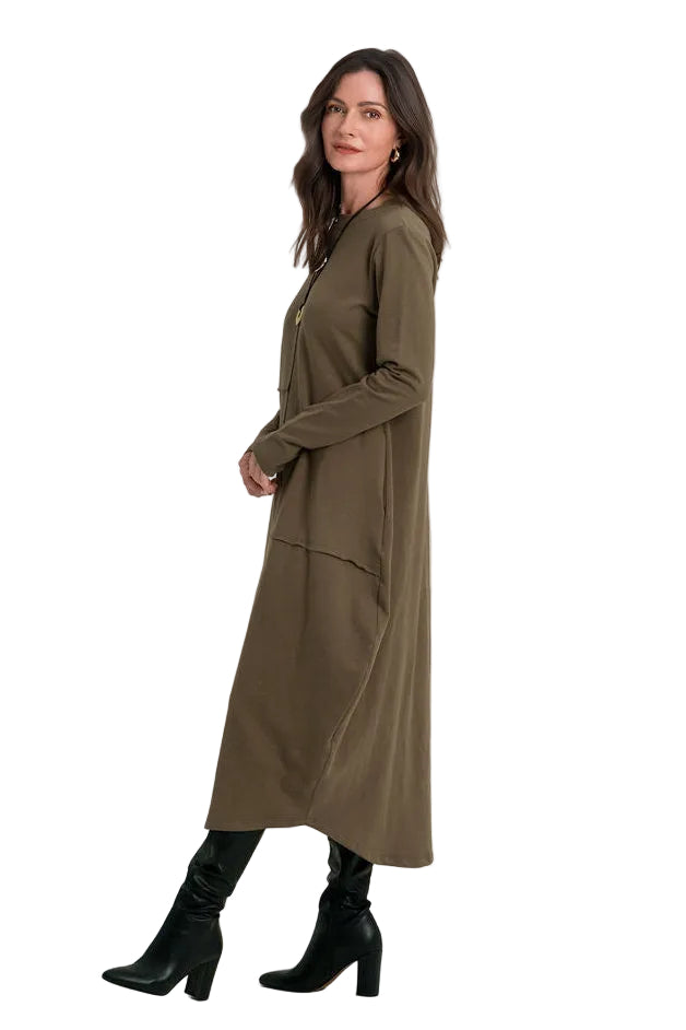 A woman modeling a 100% cotton long olive green dress with black heeled boots against a plain white studio background.