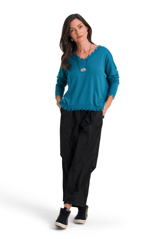 A woman modeling a teal long-sleeve pima cotton v-neck sweater and black pants against a plain white background.
